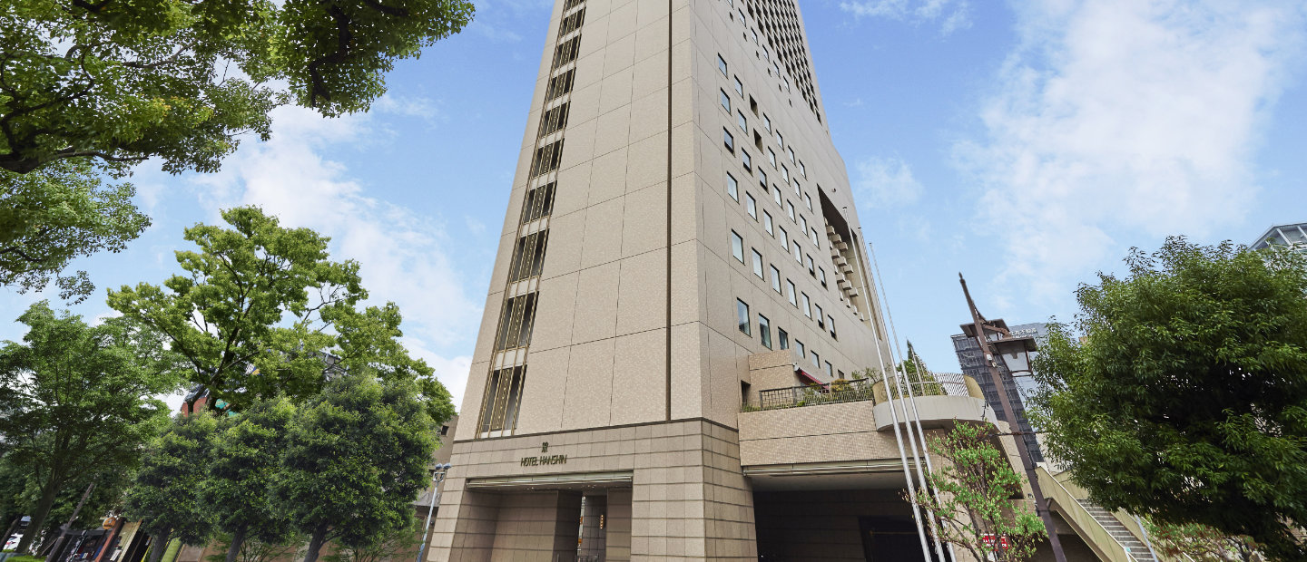 Hotel Hanshin Osaka tall building in sunny weather with green trees in the front